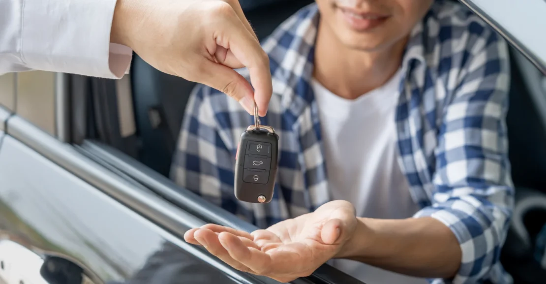 Business traveler receiving rental car keys, illustrating the choice between a car service and rental car for business travel.